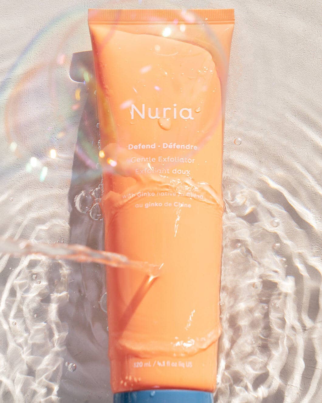 Orange bottle with white lettering in water. Title of product is Nuria Defend Gentle Exfoliator. Japanese skincare brand sold in Edina Minnesota at Juniper Skincare.