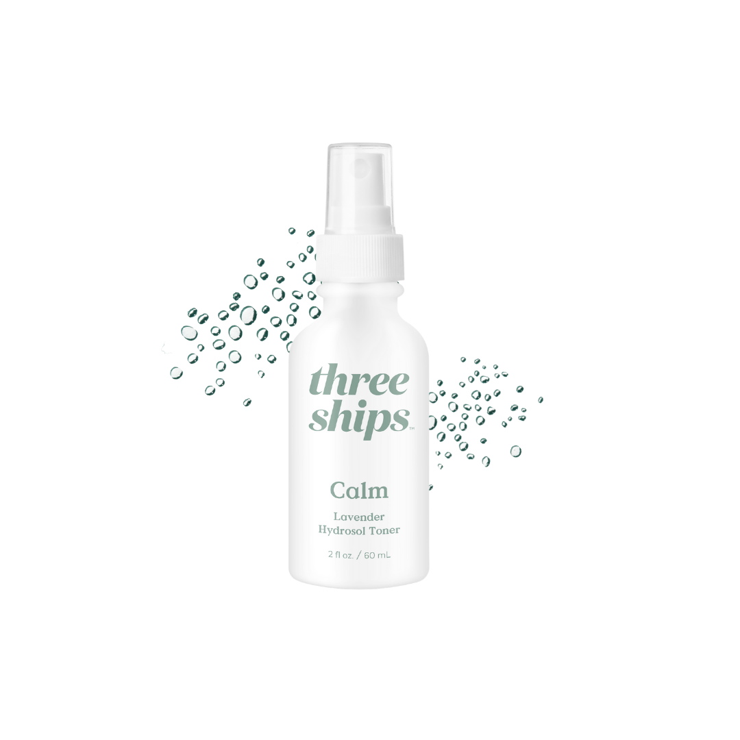 White bottle with green lettering against a white background with liquid droplets behind it. Three Ships Beauty Calm Hydrosol Toner sold at Juniper Skincare in Edina, MN.